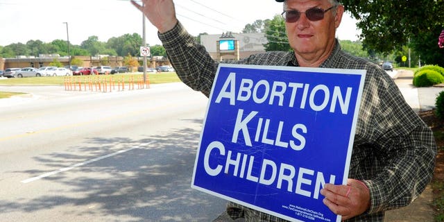 Jim Snively, of Huntsville, waves to passing cars while holding standing in front of the Alabama Women's Wellness Center, May 17, 2019. (AP Photo/Eric Schultz)