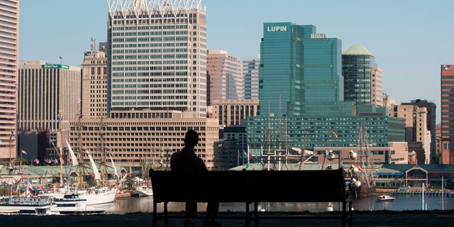 File print - a male sits on a park dais unaware Baltimore bay and skyline, Baltimore, Maryland. (Photo By: Education Images/UIG around Getty Images)