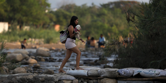 A woman holding her pet crosses illegally into Colombia near the Simon Bolivar International Bridge in La Parada near Cucuta, Colombia, Wednesday, May 1, 2019, on the border with Venezuela. The border area near Cucuta was peaceful Wednesday, even as Venezuelans heeded opposition leader Juan Guaidó's call to fill streets around the nation but security forces showed no sign of backing his cry for a widespread military uprising, instead dispersing crowds with tear gas as the political crisis threatened to deepen. (AP Photo/Fernando Vergara)