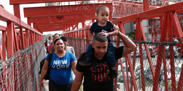 In this April 29, 2019, photo, Cuban migrants are escorted in Ciudad Juarez, Mexico, by Mexican immigration officials as they cross the Paso del Norte International bridge to be processed as asylum seekers on the U.S. side of the border. U.S. authorities have been telling asylum seekers that they are at capacity and to return when space opens up, a hands-off approach that has created haphazard and often-dubious arrangements in Mexico. (AP Photo/Christian Torres)