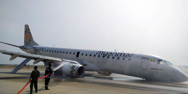 Firefighters work with hose on a plane of Myanmar National Airline (MNA) after an accident at Mandalay International airport Sunday, May 12, 2019, in Mandalay, Myanmar. All passengers and crew are reported safe and uninjured after a Myanmar National Airlines plane made a scheduled but emergency landing at Mandalay International Airport on only its rear landing wheels after the front landing gear failed to deploy.