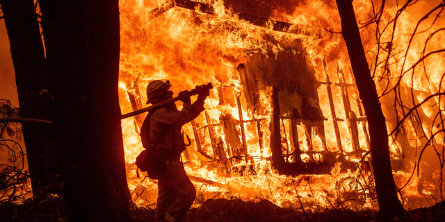 FILE - In this Nov. 9, 2018 file photo, firefighter Jose Corona sprays water as flames from the Camp Fire consume a home in Magalia, Calif. Federal officials say an effort to develop a better fire shelter following the deaths of 19 wildland firefighters in Arizona six years ago has failed. Officials at the National Interagency Fire Center in Boise in a decision on Wednesday, May 15, 2019 say the current fire shelter developed in 2002 will remain in use, saying the current shelter combines the most practical level of protection balanced against weight, bulk and durability. (AP Photo/Noah Berger, File)