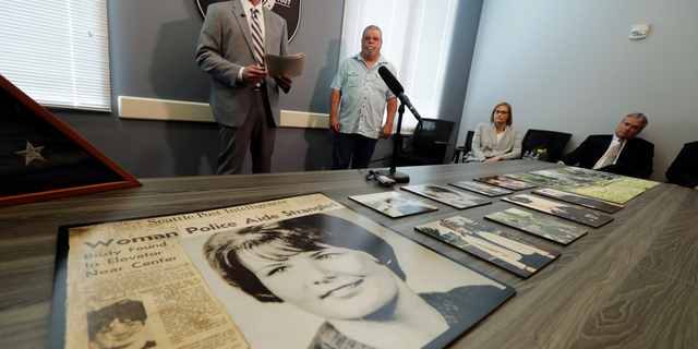Seattle Police homicide Detective Rolf Norton, left, talks to reporters near a photo of Susan Galvin, who was murdered in Seattle in 1967, Tuesday, May 7, 2019, at Seattle Police Dept. headquarters in Seattle. Police said Tuesday they have solved the cold case of the murder of Galvin with the help of DNA and a family tree -- a method that has revolutionized cold-case investigations across the U.S. Looking on is Galvin's brother, Chris Galvin, center. (AP Photo/Ted S. Warren)