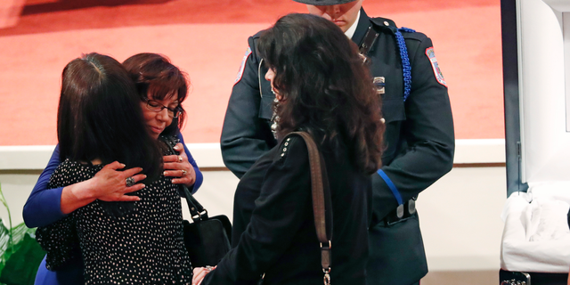 Pamela McKeithen, widow of officer Robert S. McKeithen, second from left, hugs a mourner as a member of a law enforcement agency honor guard, stands watch, as people pay their respects to McKeithen and his family in the First Baptist Church of Biloxi, Monday morning, May 13, 2019, prior to the funeral service. McKeithen was killed outside headquarters May 5. (AP Photo/Rogelio V. Solis)