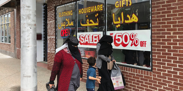 In this May 2, 2019, photo two Muslim women walk past a business in Hamtramck, Mich. The city agreed to build 200 units of single-family housing as a remedy for destroying black neighborhoods in the 1960s. Three houses still remain to be built, decades after the lawsuit was filed. It's the longest-running housing discrimination case in the U.S. Hamtramck now is much more culturally diverse. A majority of city council members are Muslim. Federal Judge Damon Keith recently died at age 96 without seeing the end of the case. (AP Photo/Ed White)