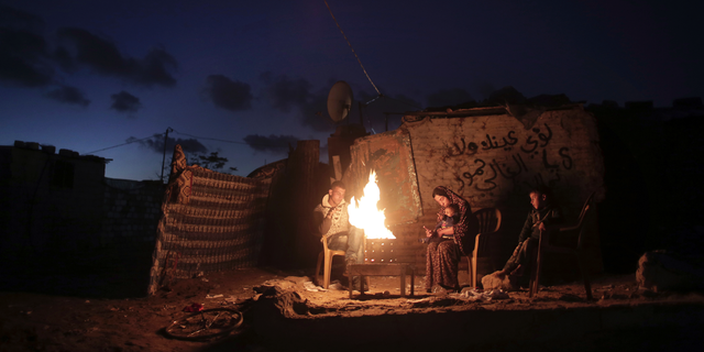 File - In this Jan. 15, 2017 file photo, a Palestinian family warm up outside their makeshift house during a power cut in Khan Younis in the southern Gaza Strip. Qatar's Foreign Ministry said Tuesday, May 7, 2019, that it will send $480 million to Palestinians in the West Bank and the Gaza Strip after a cease-fire deal ended the deadliest fighting between Israel and Palestinian factions since a 2014 war. A statement from Qatar said $300 million would support health and education programs of the Palestinian Authority, while $180 million would go toward "urgent humanitarian relief" in United Nations programs and toward electricity. (AP Photo/ Khalil Hamra, File)