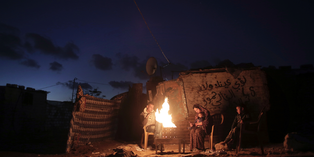 File - In this Jan. 15, 2017 file photo, a Palestinian family warm up outside their makeshift house during a power cut in Khan Younis in the southern Gaza Strip. Qatar's Foreign Ministry said Tuesday, May 7, 2019, that it will send $480 million to Palestinians in the West Bank and the Gaza Strip after a cease-fire deal ended the deadliest fighting between Israel and Palestinian factions since a 2014 war. A statement from Qatar said $300 million would support health and education programs of the Palestinian Authority, while $180 million would go toward "urgent humanitarian relief" in United Nations programs and toward electricity. (AP Photo/ Khalil Hamra, File)