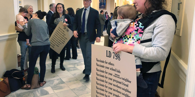 Kate Herrold, of Falmouth, holds her daughter with other mothers in a hallway, Thursday, May 2, 2019, at the Statehouse in Augusta, Maine, where the Senate passed a bill ending non-medical vaccine exemptions. The bill would end religious and philosophical opt-outs by 2021 for public school students, as well as employees at nursery schools and health care facilities. It faces further legislative action in both chambers. (AP Photo/Marina Villeneuve)