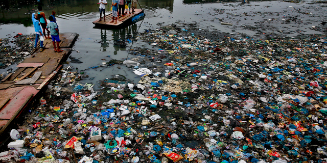FILE - In this Sunday, Oct. 2, 2016 file photo, a man guides a raft through a polluted canal littered with plastic bags and other garbage in Mumbai, India. United Nations officials say nearly all of the world's countries have agreed on a deal to better manage plastic waste, with the United States a notable exception. A "legally binding framework" that affects thousands of types of plastic waste emerged Friday, May 10, 2019 after a two-week meeting of U.N.-backed conventions on plastic waste and toxic chemicals. (AP Photo/Rafiq Maqbool, file)