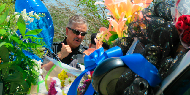 A Biloxi police vehicle that was assigned to patrolman Robert McKeithen is covered in flowers as Biloxi Police Capt. Milton Houseman, rear, talks , with a member of the Combat Veterans Motorcycle Association, Tuesday, May 7, 2019, in Biloxi, Moss. Houseman said he was one of the officers who brought Darian Tawan Atkinson, 19, to Biloxi after his arrest in Wiggins on May 6, in the death of Patrolman McKeithen. (AP Photo/Janet McConnaughey)