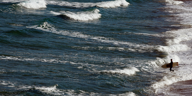 A surfer goes to the Atlantic sea in Biarritz, southwestern France, Tuesday May 14, 2019. Temperatures in southwestern France reached 20 degrees Celsius (68 Fahrenheit). (AP Photo/Bob Edme)