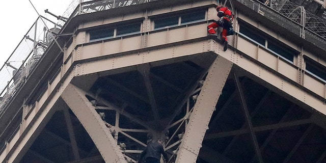 A rescue worker, top in red, hangs from the Eiffel Tower while a climber is seen below him between two iron columns Monday, May 20, 2019 in Paris.