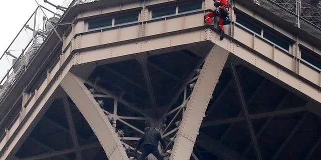 A rescue worker, top in red, hangs from the Eiffel Tower while a climber is seen below him between two iron columns Monday, May 20, 2019 in Paris.