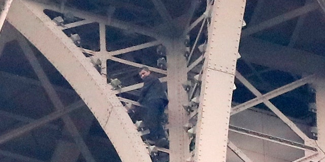 A climber is pictured between two iron columns of the Eiffel Tower while a rescue worker is partially seen at right, Monday, May 20, 2019 in Paris.
