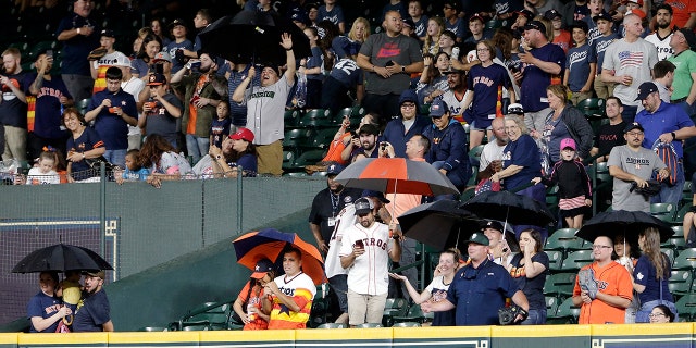Fans sitting behind right field pull out umbrellas as rain seeps through gaps in the roof of Minute Maid Park during the eighth inning of a baseball game between the Texas Rangers and the Astros on Thursday, May 9, 2019, in Houston.