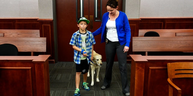 Pella is seen here in 2016 with one of the children who helped train her, as well as handler Amber Urban.