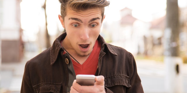 Young shocked man receiving news on smartphone and looking shocked while standing on street