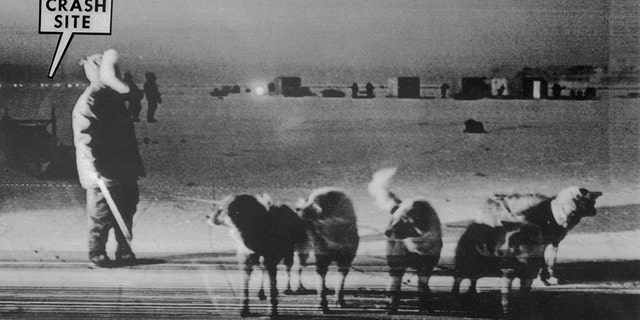 An Eskimo dog team stands on frozen Baffin Bay near the site of the crash of a U.S. B-52 nuclear bomber on January 21, 1968. Buildings on the right are recovery teams. A string of lights at left marks the crash site.