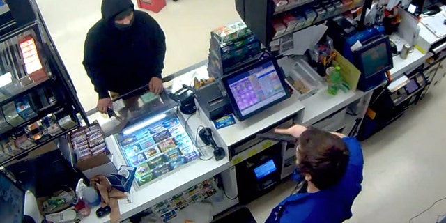 Image from surveillance video showing a convenience store in Oregon pulling out a gun on a masked would-be robber who had a hatchet.