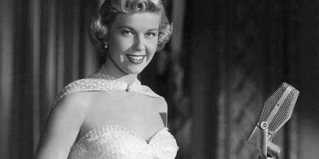 A promotional portrait of American singer and actor Doris Day smiling as she stands behind a microphone, from director Michael Curtiz's film, "Young Man with a Horn."