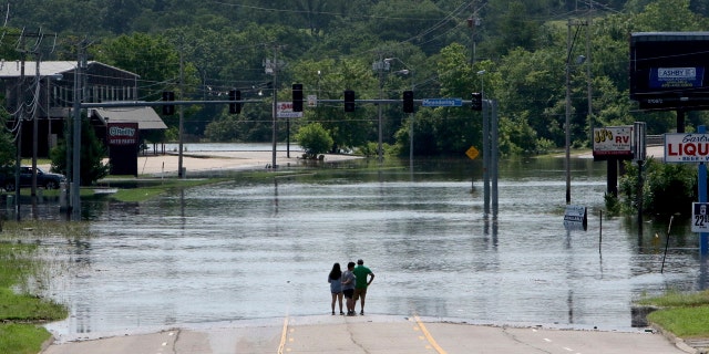 People stand in the middle of Rogers Avenue and look out over the flooded Massard Creek at the intersection of Meandering Way and Rogers Avenue, in Fort Smith, Ark., Saturday, May 25, 2019.