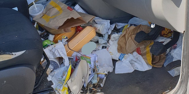 In the image, McDonald’s wrappers and cups, Styrofoam containers, receipts, documents and various other indiscernible pieces of garbage can be seen spilling out of the driver’s side cab, on the dash and behind the driver pedals.