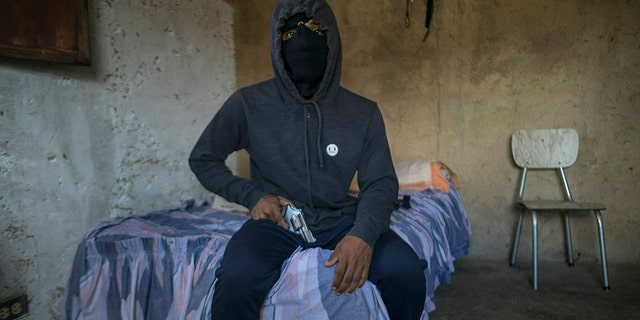 A masked gangster who goes by the nickname "El Negrito" poses for a portrait with his gun inside his gang's safe-house in the Petare slum of Caracas, Venezuela, Monday, May 13, 2019. The 24-year-old, who says he’s lost track of his murder count, is quick to gripe about how Venezuela’s failing economy is cutting into his profits and has considered leaving the trade in Venezuela and emigrating. (AP Photo/Rodrigo Abd)
