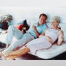 Rock Hudson (1925-1985), US actor, wearing white trousers and a light blue short-sleeved shirt, and Doris Day, US singer and actress, in a pink gingham dress, both reclining on a sofa, laughing and holding drinks, circa 1960. (Photo by Silver Screen Collection/Getty Images)