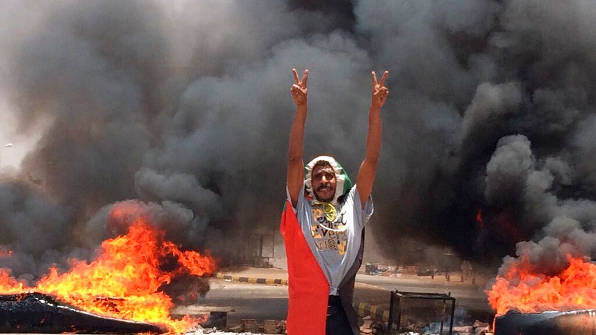 In this Monday, June 3, 2019 file photo, a protester flashes the victory sign in front of burning tires and debris on road 60, near Khartoum's army headquarters, in Khartoum, Sudan, Monday, June 3.