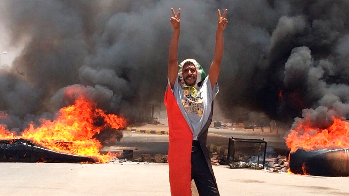 In this Monday, June 3, 2019 file photo, a protester flashes the victory sign in front of burning tires and debris on road 60, near Khartoum's army headquarters, in Khartoum, Sudan, Monday, June 3.