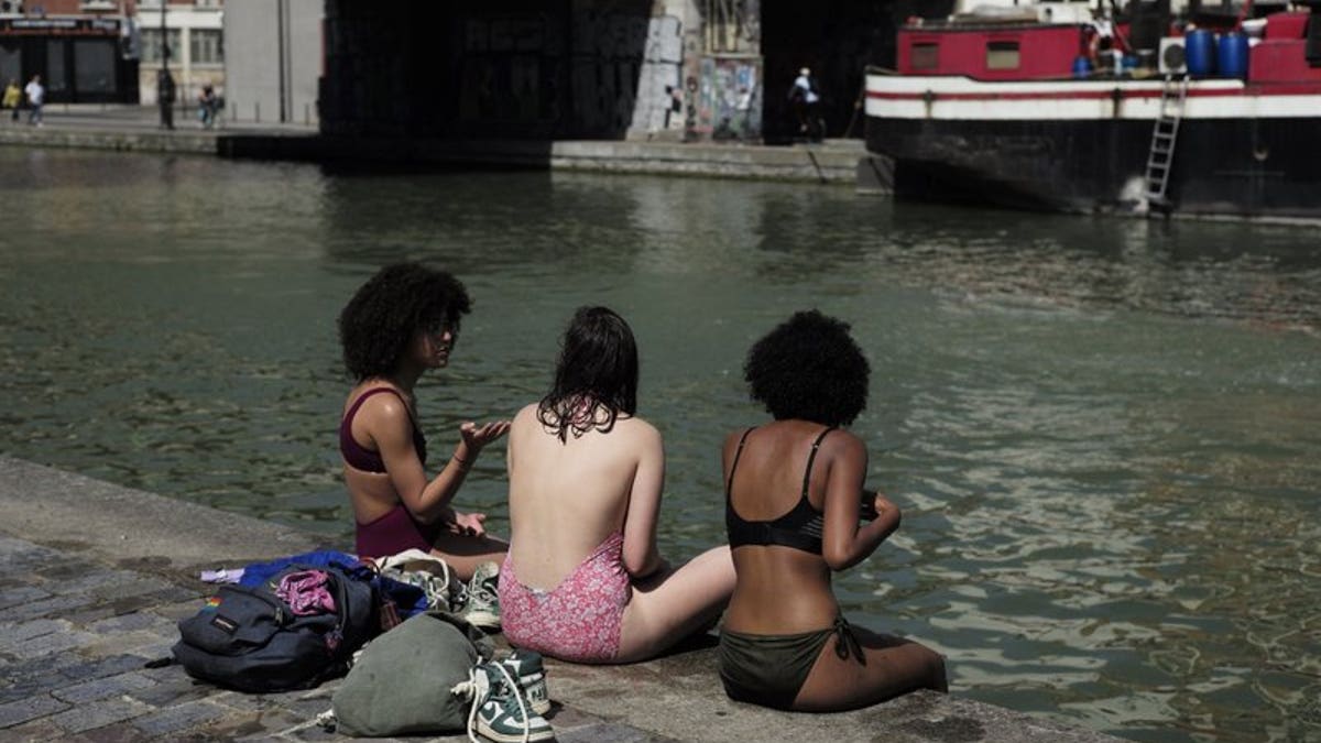 Girls wearing swimsuits sit along the Canal de l'Ourcq in Paris, Friday, June 28, 2019. Schools are spraying kids with water and nursing homes are equipping the elderly with hydration sensors as France and other nations battle a record-setting heat wave baking much of Europe.