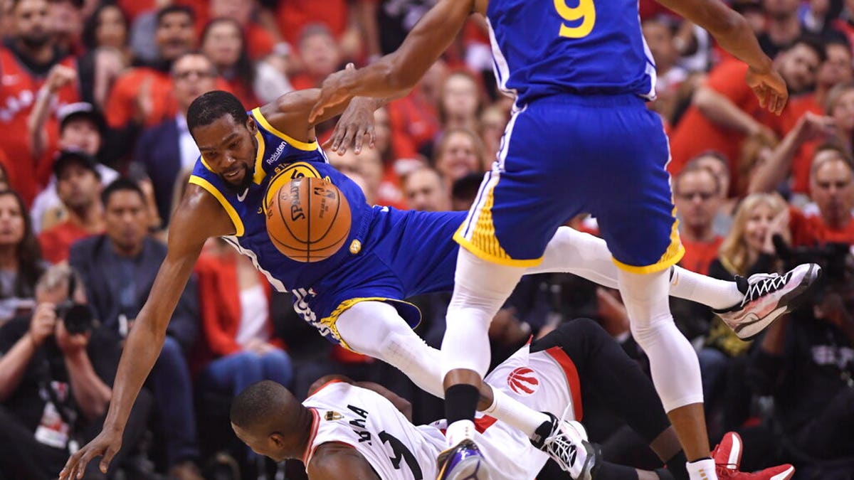 Golden State Warriors forward Kevin Durant, left, falls over Toronto Raptors center Serge Ibaka, bottom, as Warriors forward Andre Iguodala (9) looks on during first-half basketball game action in Game 5.
