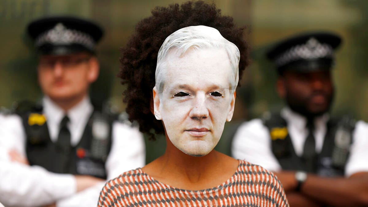 Police watch an Assange supporter wearing a mask and protesting at Westminster Magistrates Court in London, Friday, June 14, 2019. WikiLeaks founder Julian Assange is expected to appear at hearing in a London court via video link as he continues his fight against extradition to the United States.
