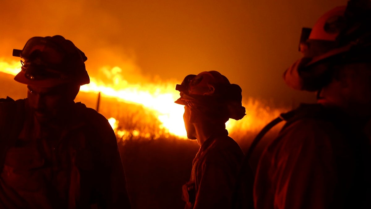 In this Sept. 12, 2015 file photo, California Department of Corrections and Rehabilitation inmates stand guard as flames from the Butte Fire approach a containment line near San Andreas, Calif. Attorneys representing 14 local governments said Tuesday, June 18, 2019 that they had reached a $1 billion settlement with California utility Pacific Gas &amp; Electric for a series of fires dating to 2015. (AP Photo/Rich Pedroncelli, File)