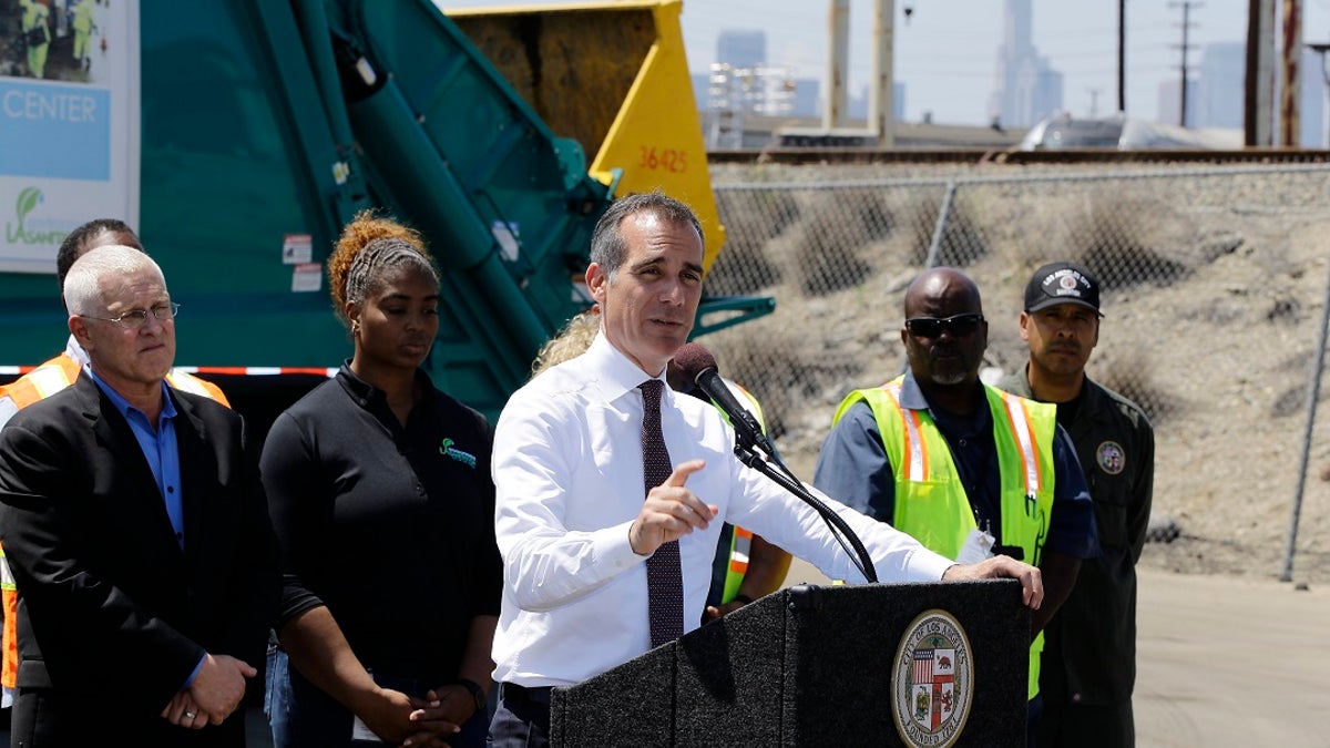 Los Angeles Mayor Eric Garcetti, at podium, surrounded by city sanitation workers, speaks about the city's homelessness problem at a news conference in Los Angeles on June 19, 2019. Far left, is city councilman, Mike Bonin. (AP Photo/Damian Dovarganes)