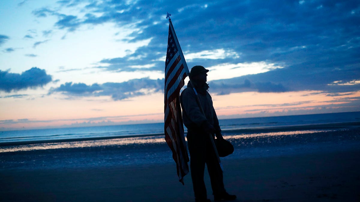 Udo Hartung from Frankfurt, Germany, a World War II reenactor, holds the U.S. flag as he stands at dawn on Omaha Beach, in Normandy, France on Thursday. (AP)