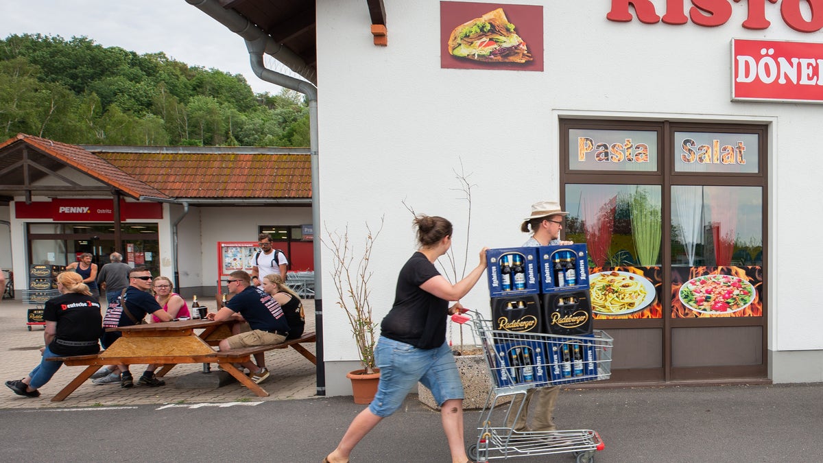 A woman and a man push a shopping cart with beer crates along the street near a local supermarket to protest the Shield and Sword Festival.  (Photo by Daniel Schäfer/picture alliance via Getty Images)