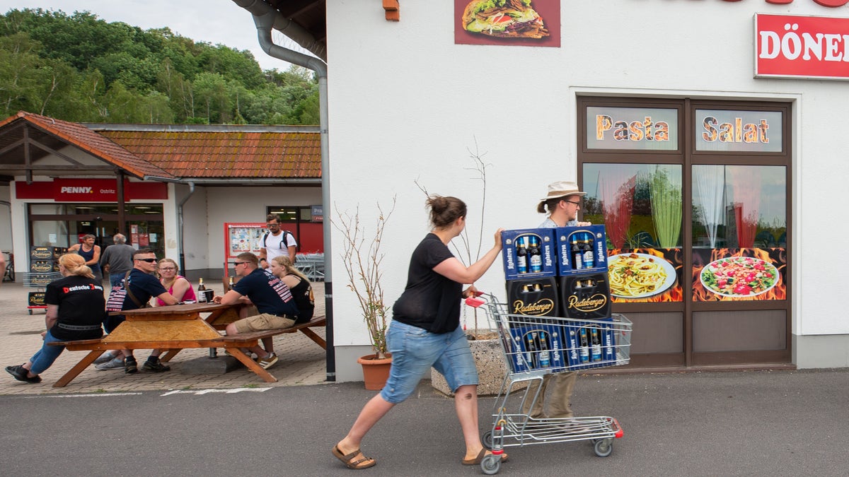 A woman and a man push a shopping cart with beer crates along the street near a local supermarket to protest the Shield and Sword Festival. (Photo by Daniel Schäfer/picture alliance via Getty Images)