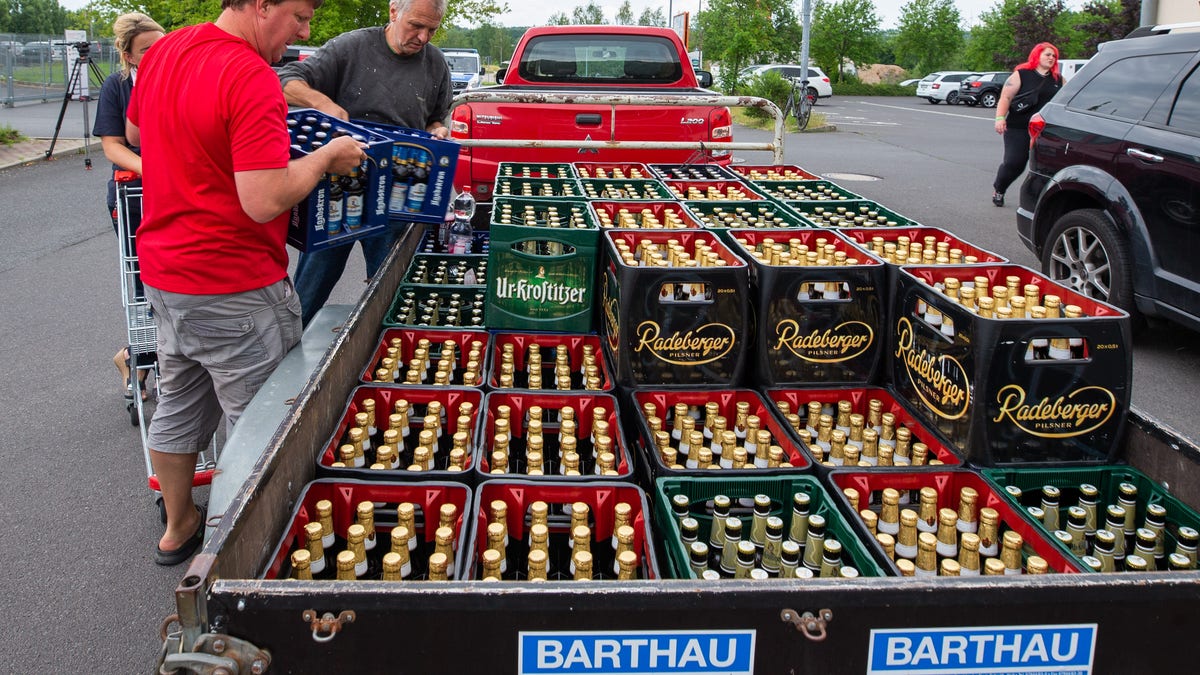  A woman and two men load beer crates near a local supermarket onto a trailer.  (Photo by Daniel Schäfer/picture alliance via Getty Images)