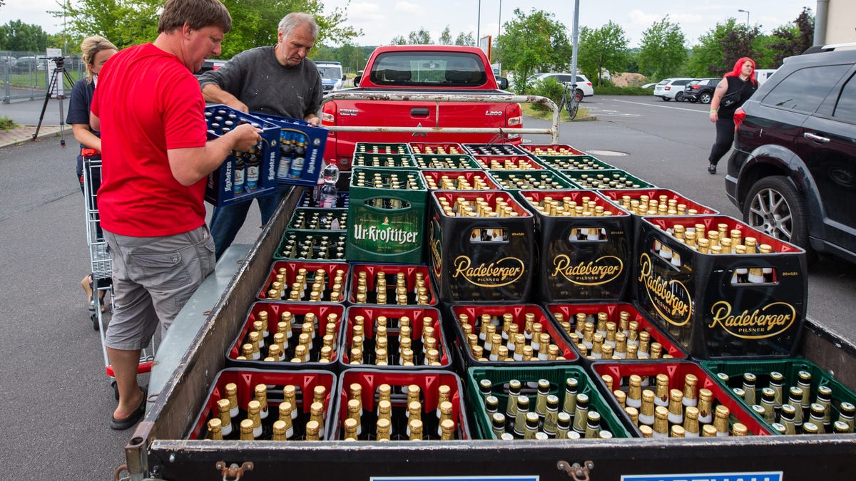 A woman and two men load beer crates near a local supermarket onto a trailer. (Photo by Daniel Schäfer/picture alliance via Getty Images)