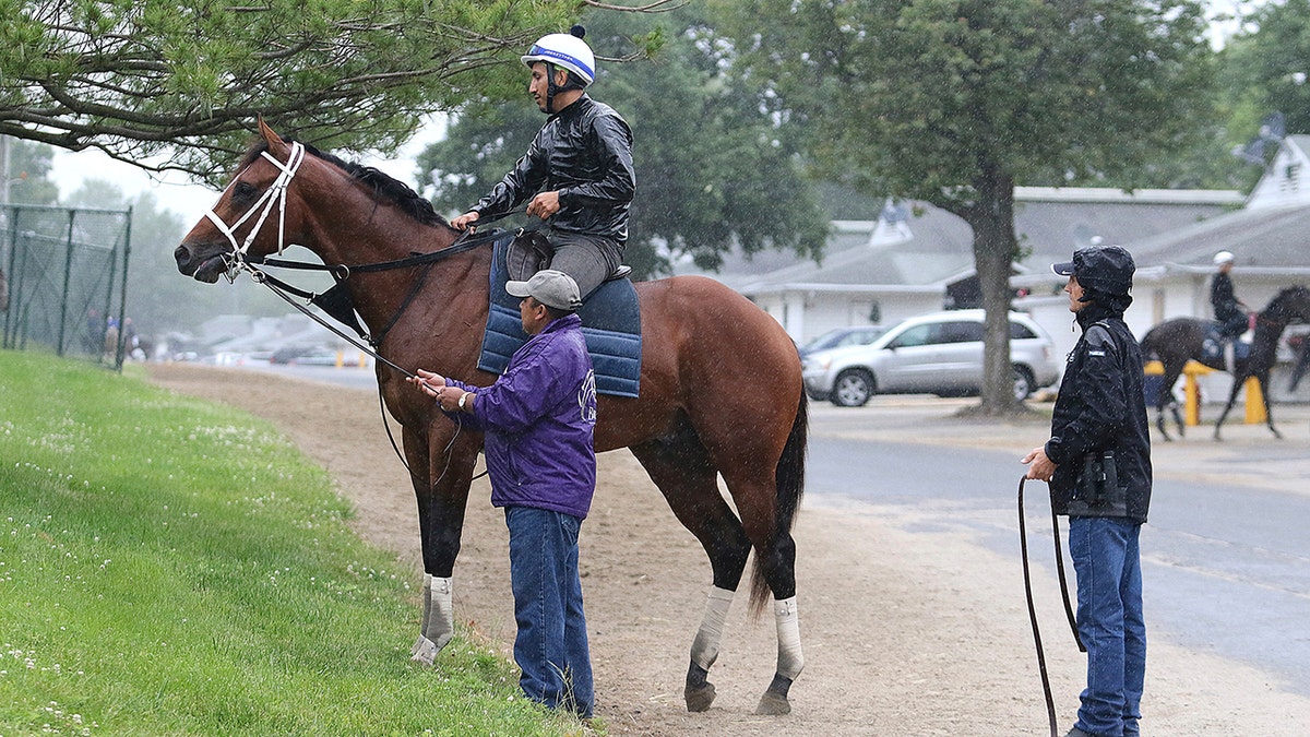 Maximum Security, ridden by exercise rider Edelberto Rivas up, pauses after a morning gallop as assistant trainer Jose Hernandez and Jason Servis, right, to look on at Monmouth Park, Thursday, June 13, 2019, in Oceanport, N.J. Maximum Security will make his next start in Sunday's $150,000 Pegasus Stakes horse race at the track. (Bill Denver/EQUI-PHOTO via AP)