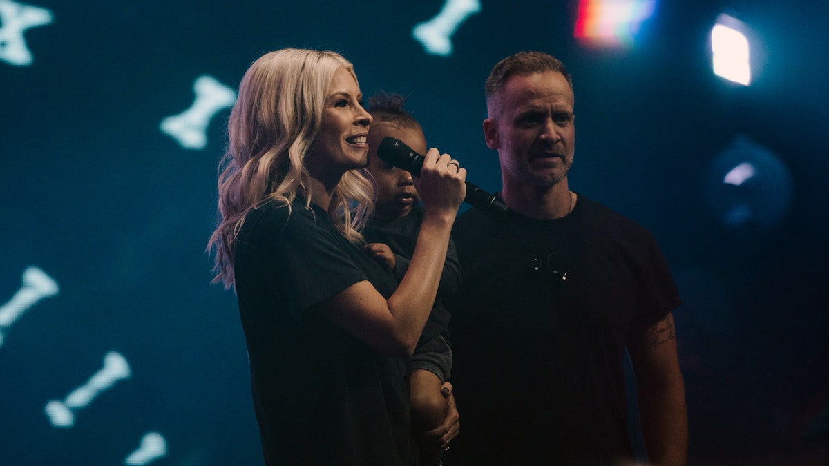 Jenn Johnson speaks on the opening night of "Heaven Come" in downtown Los Angeles May 23, 2019, holding her adopted son, Ryder Moses, and alongside her husband, Brian.