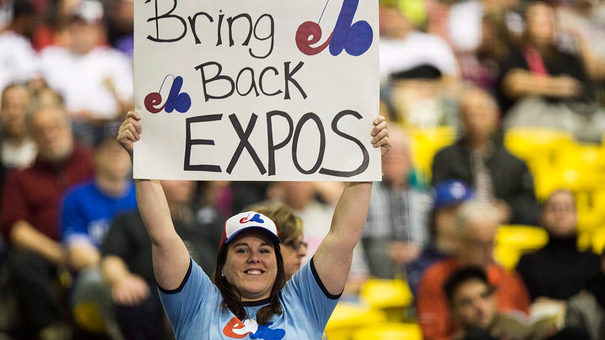 FILE - In this April 3, 2015, file photo, a fan holds up a sign during a pregame ceremony as the Toronto Blue Jays face the Cincinnati Reds in an exhibition baseball game in Montreal. The Tampa Bay Rays have received permission from Major League Baseball's executive council to explore a plan that could see the team split its home games between the Tampa Bay area and Montreal. (Paul Chiasson/The Canadian Press via AP, File)