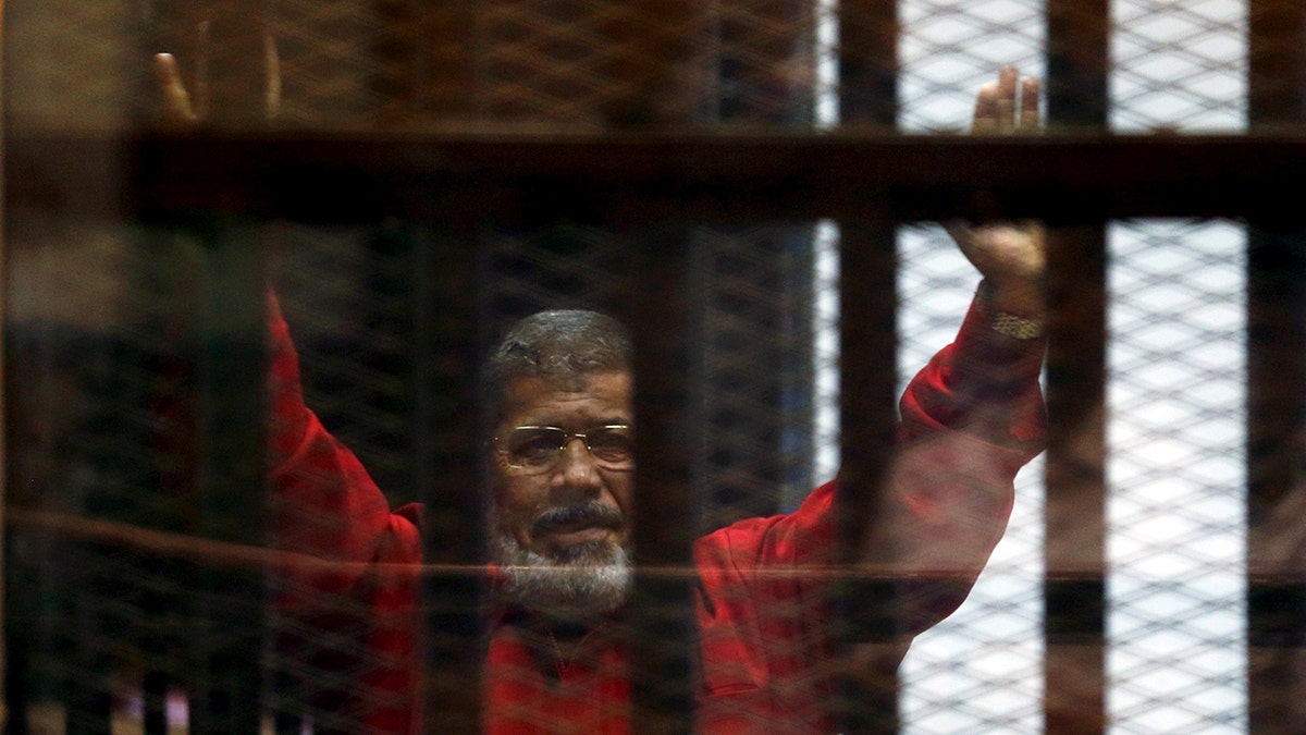 In this 2015 photo, Egypt's deposed president Mohamed Mursi greets his lawyers and people from behind bars at a court hearing.