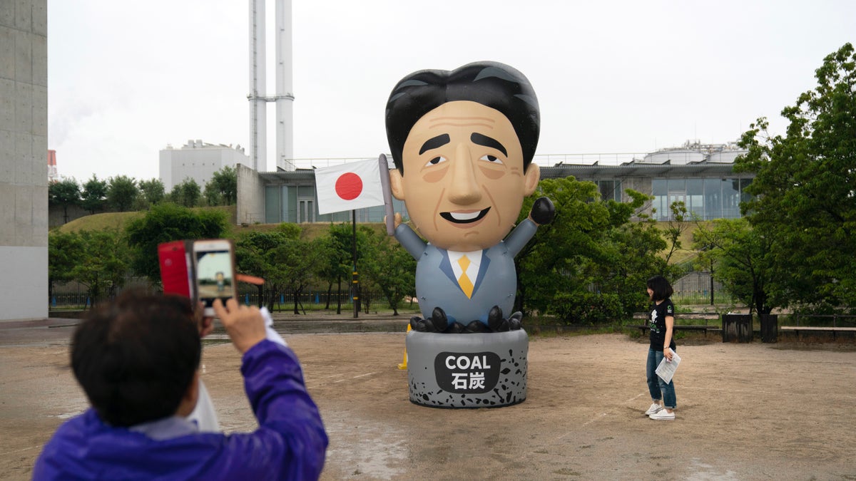 A large inflatable depicting Japanese Prime Minister Shinzo Abe stands in front of a coal-fired power plant during a priests held to demand an to coal funding ahead of the G20 Summit Thursday, June 27, 2019, in Kobe, Japan. (AP Photo/Jae C. Hong)