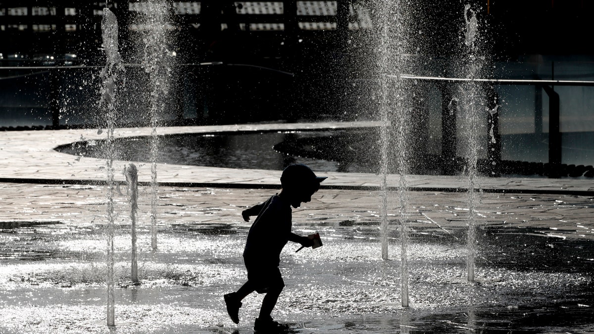 A children plays and cool-off as water sprinkles from a fountain, in Milan, Italy, Monday, June 24, 2019.