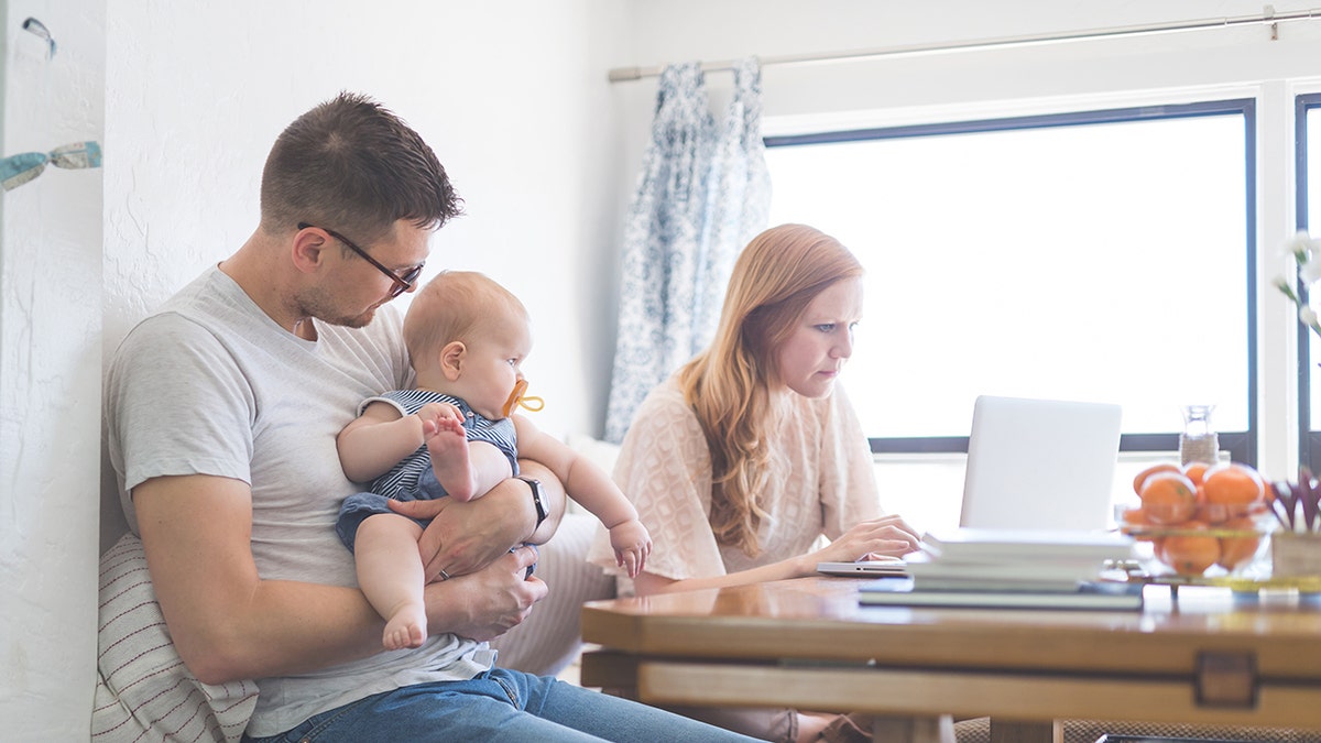 Mother checks her email while father holds baby