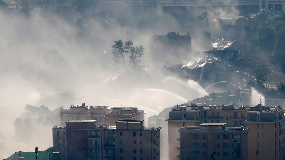 Fire hoses spray water to reduce dust triggered by the planned blast which demolished the remaining spans of the Morandi bridge, in Genoa, Italy, Friday, June 28, 2019. (AP Photo/Antonio Calanni)