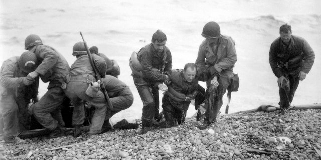 FILE - In this file photo from June 6, 1944, members of an American landing unit help their comrades ashore during the Normandy invasion. The men reached the zone code-named Utah Beach, near Sainte- Mere-Eglise, on a life raft after their landing craft was hit and sunk by German coastal defenses. (Louis Weintraub/Pool Photo via AP, File)