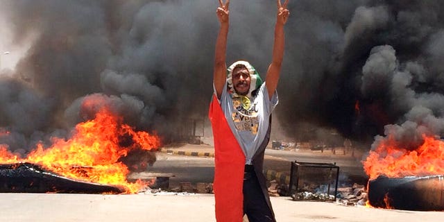 In this Monday, June 3, 2019 file photo, a protester flashes the victory sign in front of burning tires and debris on road 60, near Khartoum's army headquarters, in Khartoum, Sudan, Monday, June 3.